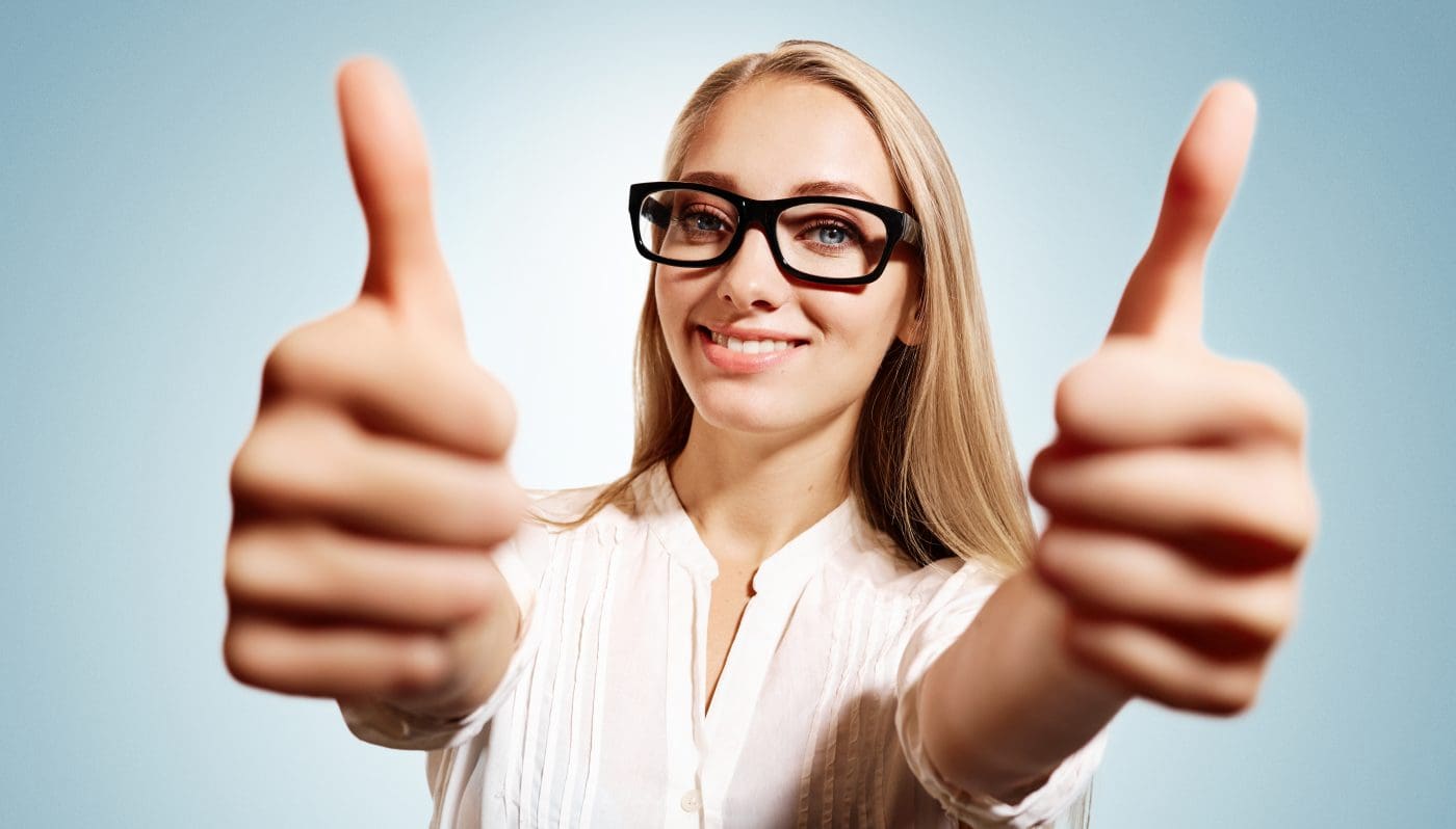 Closeup portrait handsome young smiling blonde business woman, corporate employee giving thumbs up sign at camera at blue background. Positive human emotions, facial expression, feelings.